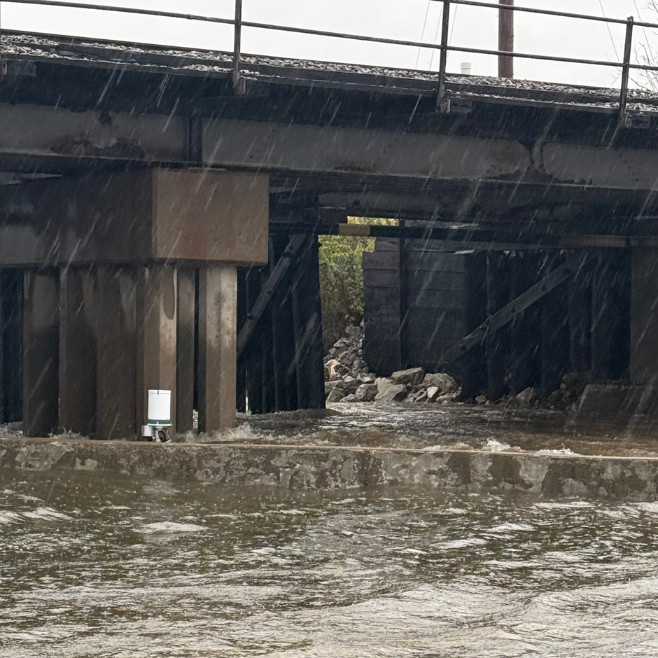 A bridge with a rushing river below it and a flood monitoring system.