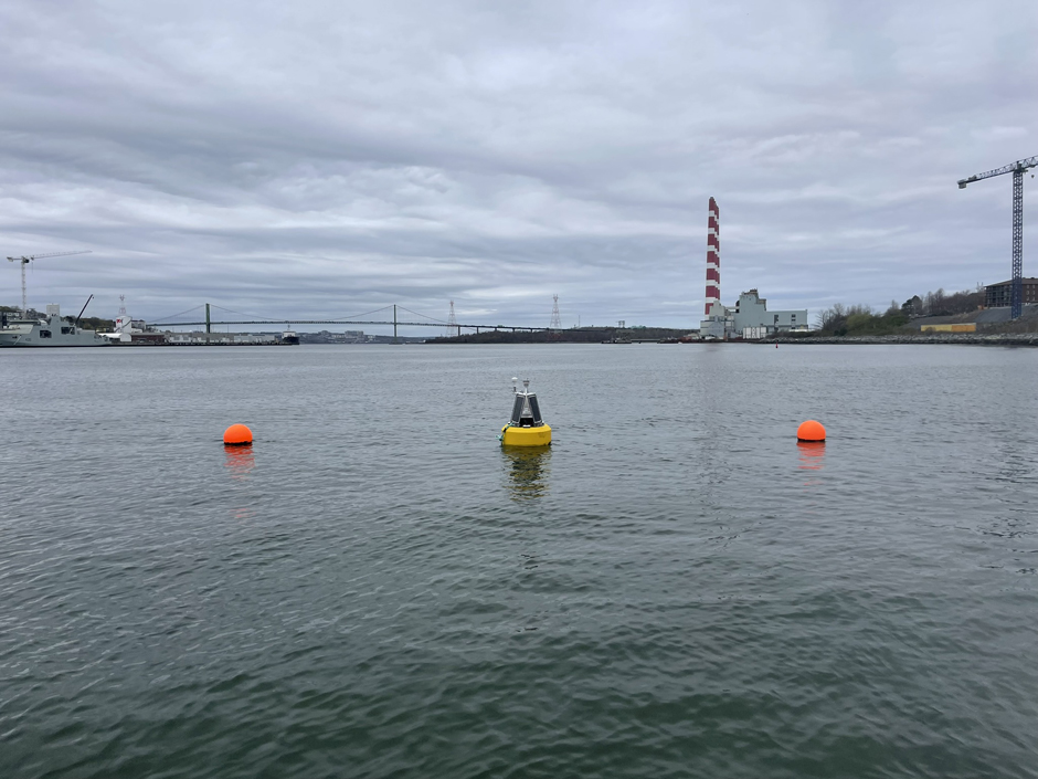 A NexSens buoy sits in Halifax Harbor, with the chimneys from the power generation station visible in the background.