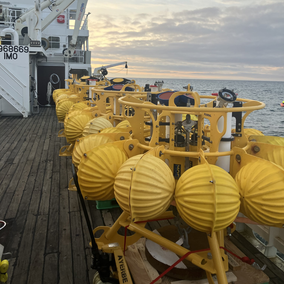 A set of ocean bottom tripods awaits deployment on the back deck of the R/V Þórunn Þórðardóttir (Iceland). Upward-looking ADCPs are visible on each tripod. Yellow spheres provide flotation for mooring recovery when the anchor is released after a year of deployment.