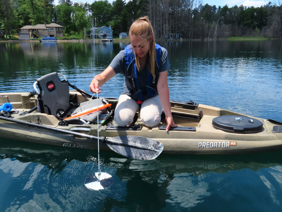 A volunteer lowers a Secchi disc to measure the water clarity of the lake.