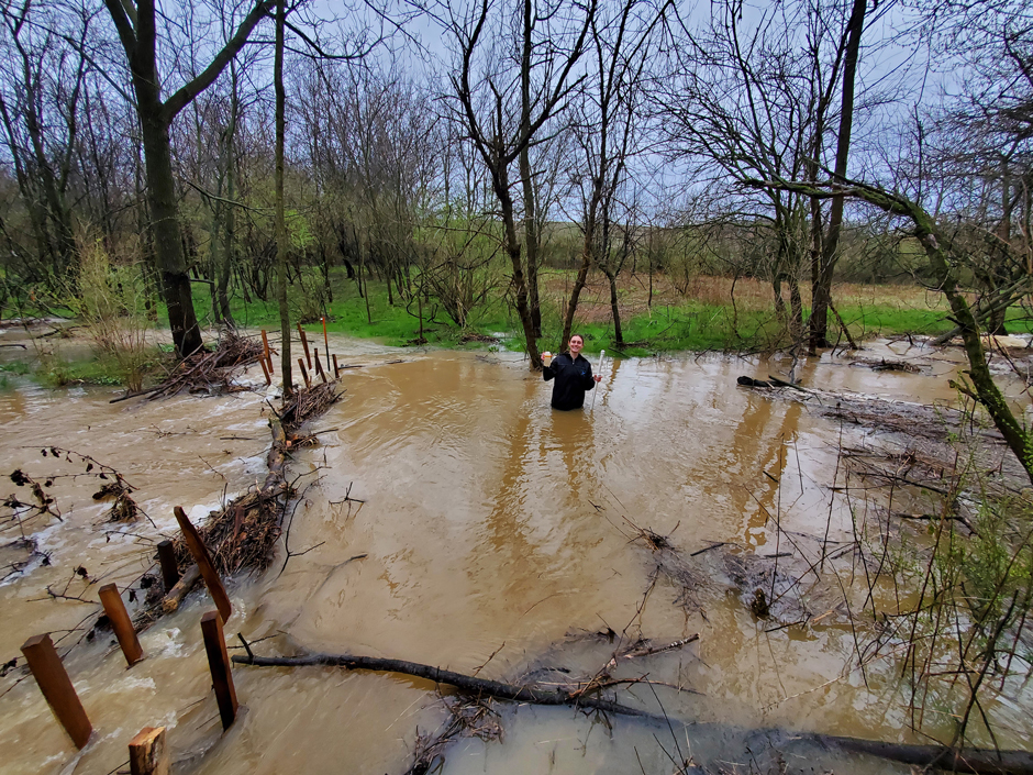 Alyana Krempa sampling water during a major storm with water flowing onto the floodplain behind her.