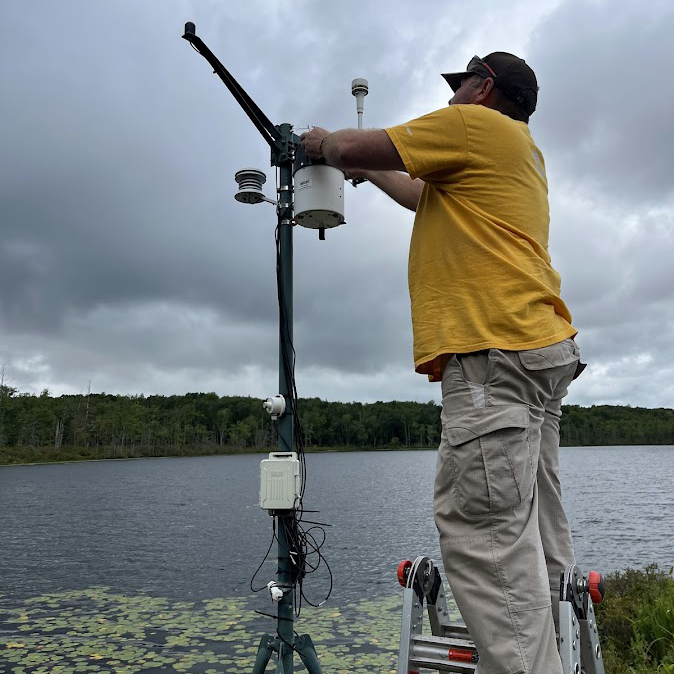 An employee at Lacawac Sanctuary in Lake Ariel, PA, working on an Onset weather station deployed on a dock at the lake.